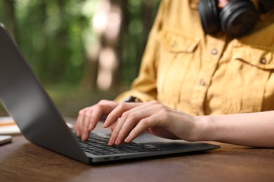 Photo of Freelancer working with laptop at wooden table outdoors, closeup. Remote job