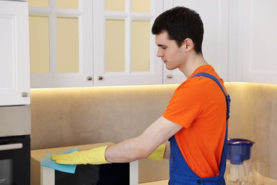 Photo of Professional janitor wearing uniform cleaning microwave oven in kitchen