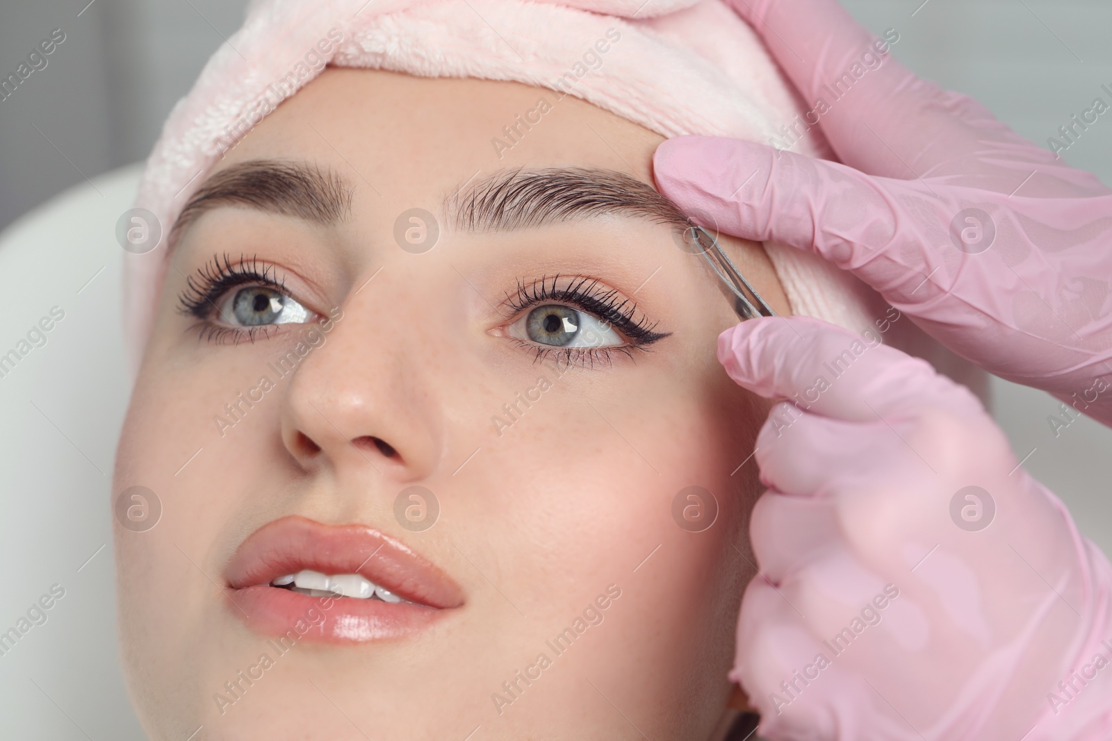 Photo of Beautician plucking young woman's eyebrow in beauty salon, closeup