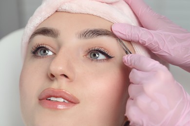 Photo of Beautician plucking young woman's eyebrow in beauty salon, closeup