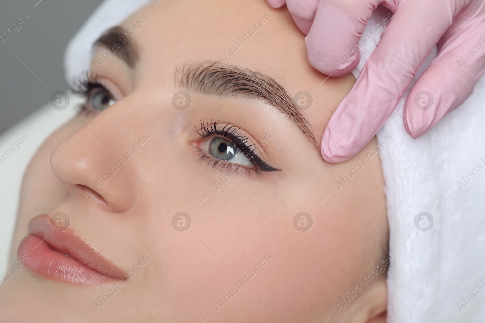 Photo of Beautician plucking young woman's eyebrow in beauty salon, closeup