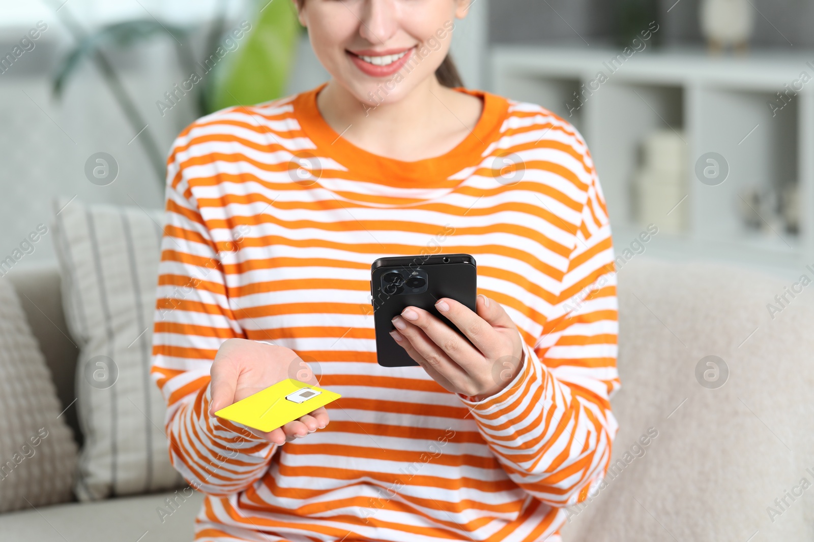 Photo of Woman holding SIM card and smartphone on sofa indoors, closeup