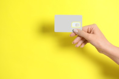 Photo of Woman holding SIM card on yellow background, closeup. Space for text