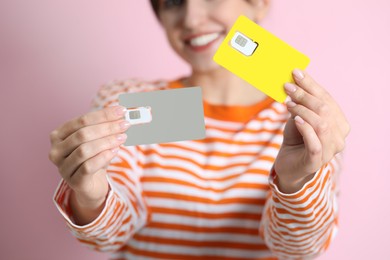 Photo of Woman holding SIM cards on pink background, closeup