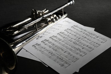 Photo of Closeup view of shiny trumpet and music sheets on dark background. Wind musical instrument