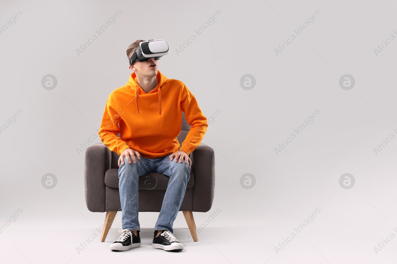 Photo of Emotional young man with virtual reality headset sitting on armchair against light grey background, space for text