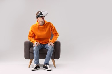 Photo of Emotional young man with virtual reality headset sitting on armchair against light grey background, space for text