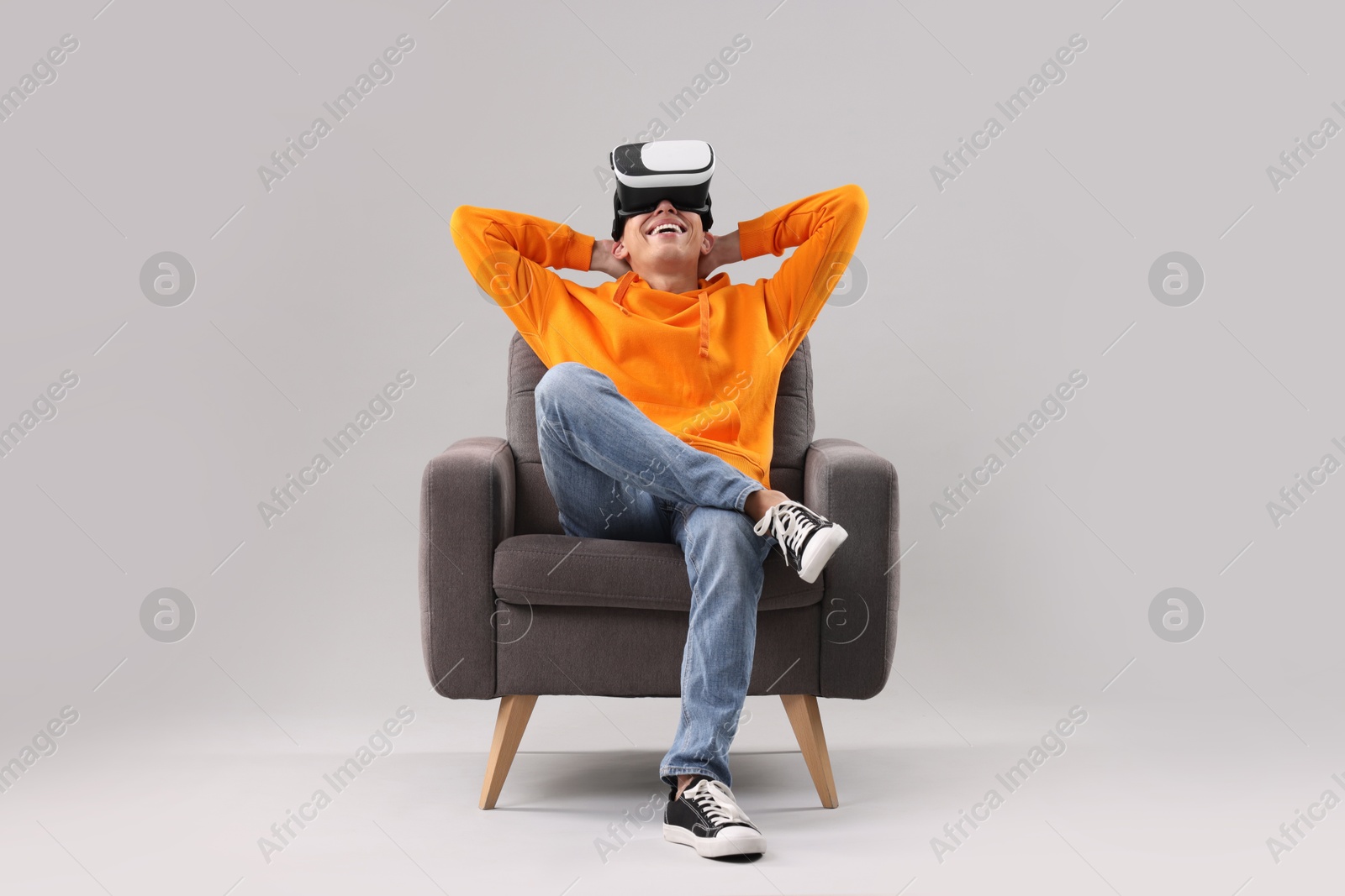 Photo of Happy young man with virtual reality headset sitting on armchair against light grey background