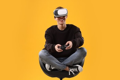 Photo of Happy young man with virtual reality headset and controller sitting on chair against yellow background