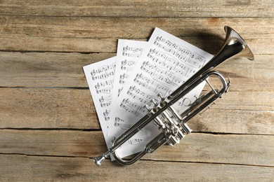 Trumpet and music sheets on wooden table, top view