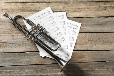 Trumpet and music sheets on wooden table, top view