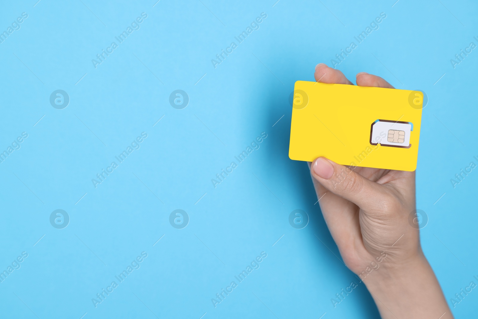 Photo of Woman holding SIM card on light blue background, closeup. Space for text