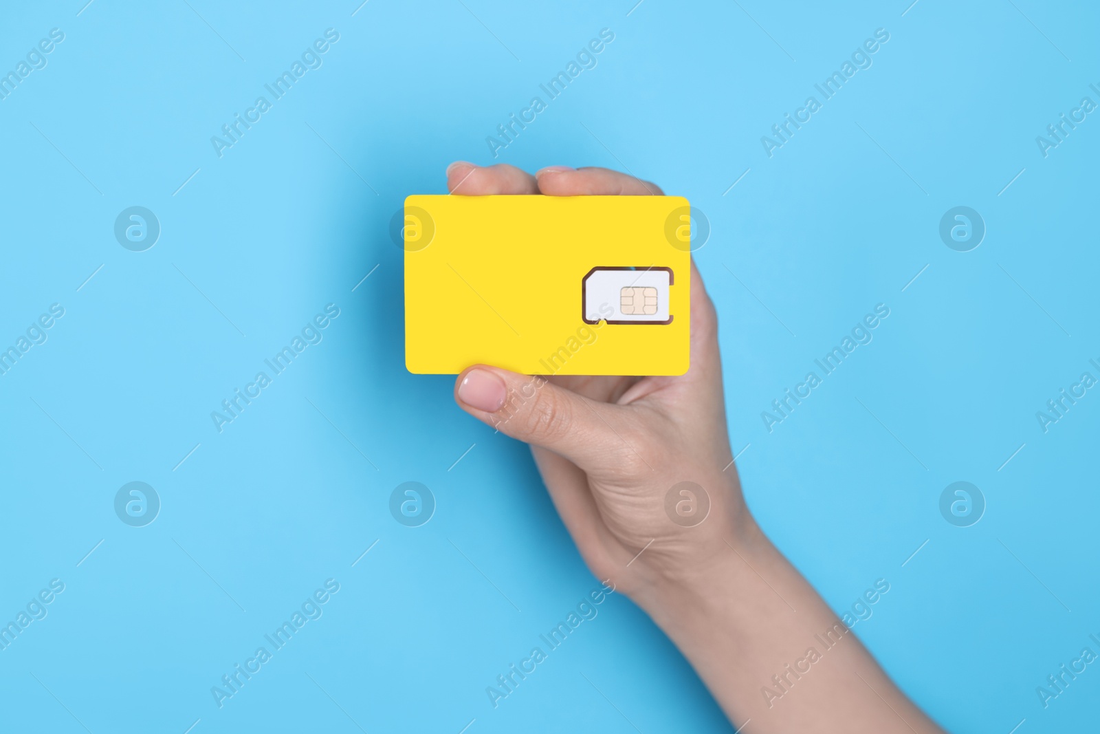 Photo of Woman holding SIM card on light blue background, closeup