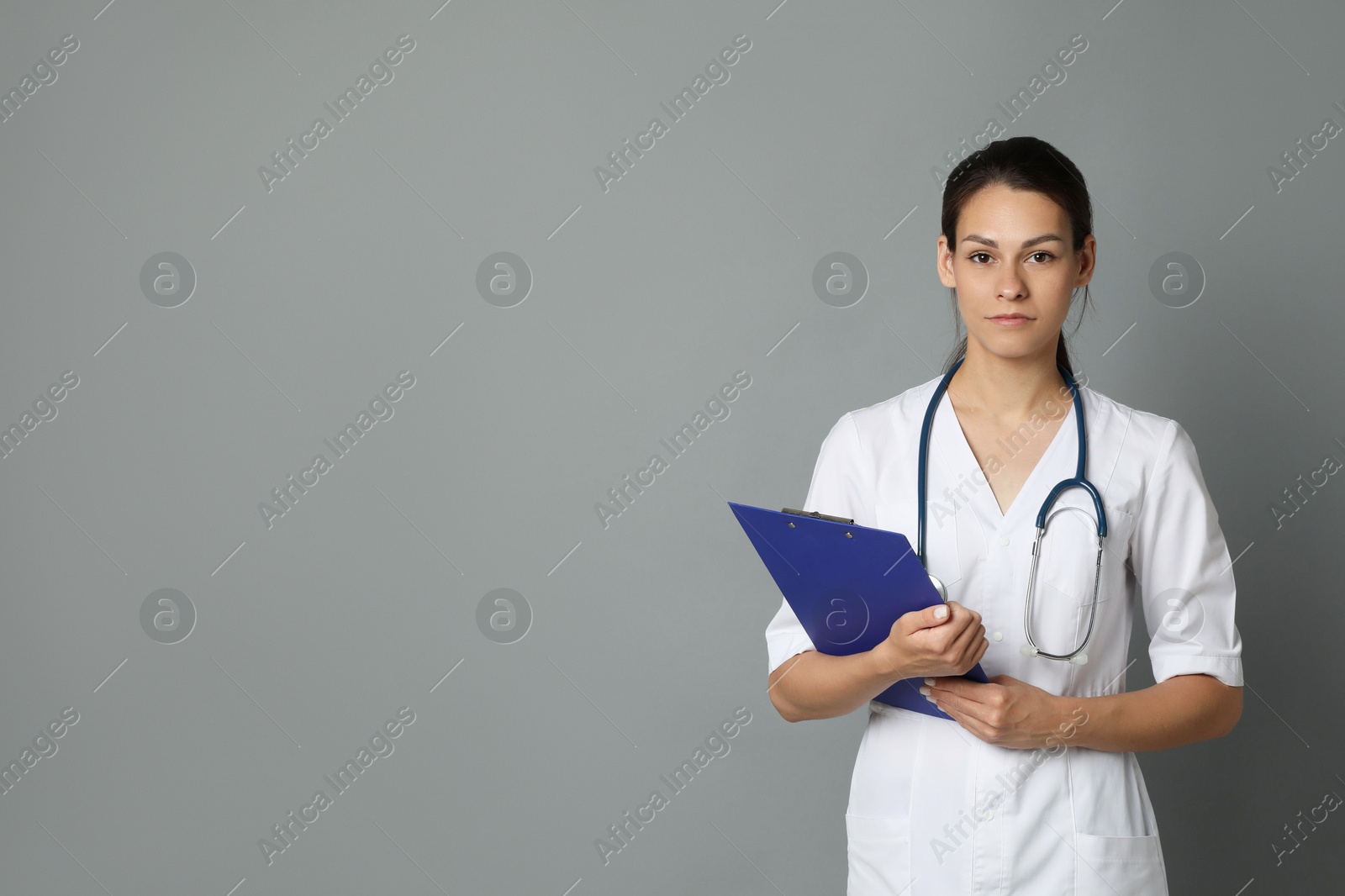 Photo of Portrait of beautiful nurse with clipboard on grey background. Space for text