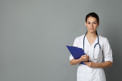 Portrait of beautiful nurse with clipboard on grey background. Space for text