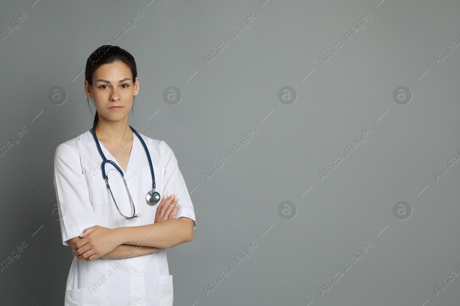 Photo of Portrait of beautiful nurse with crossed arms on grey background. Space for text