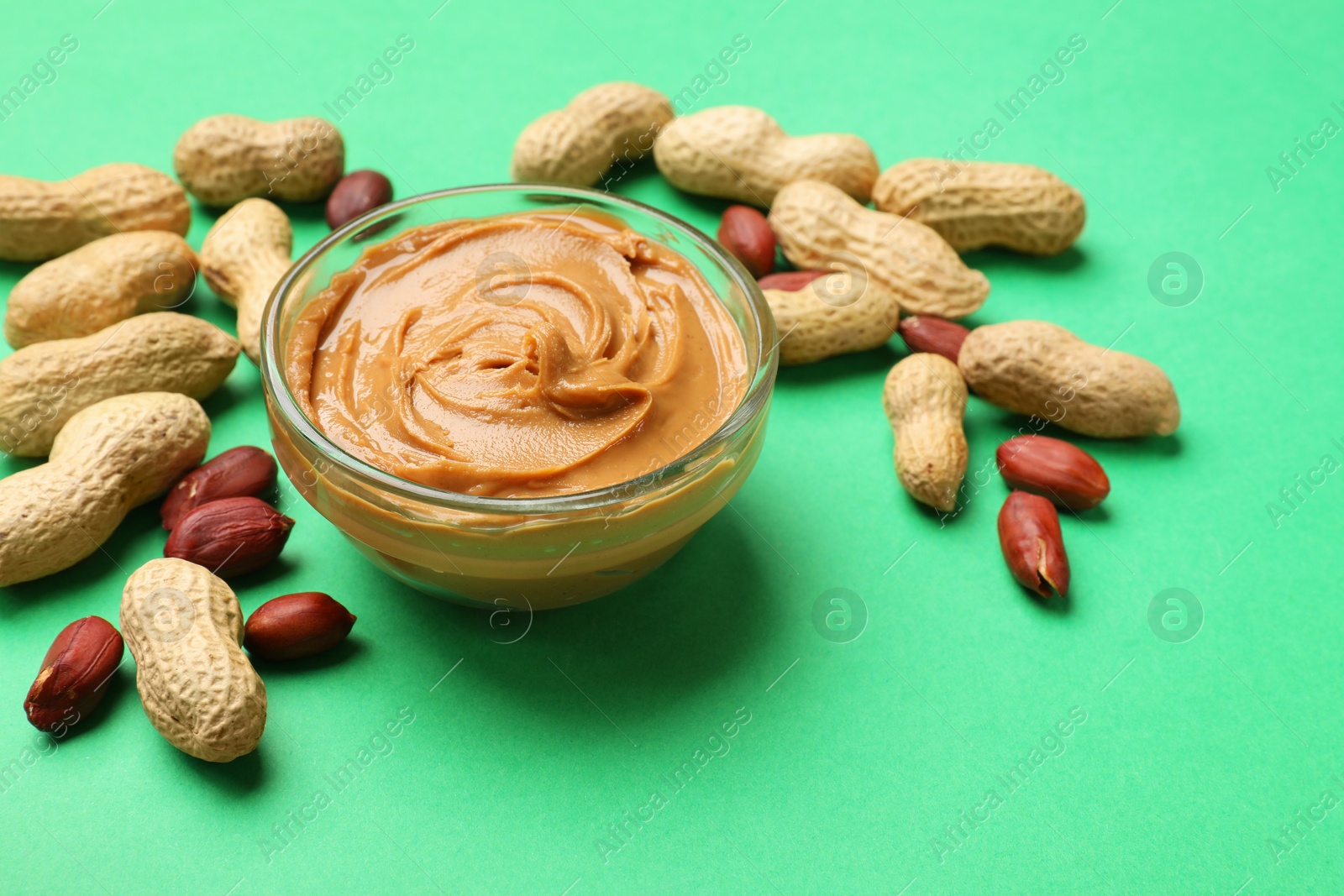 Photo of Tasty peanut butter in bowl and groundnuts on green background