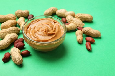 Photo of Tasty peanut butter in bowl and groundnuts on green background