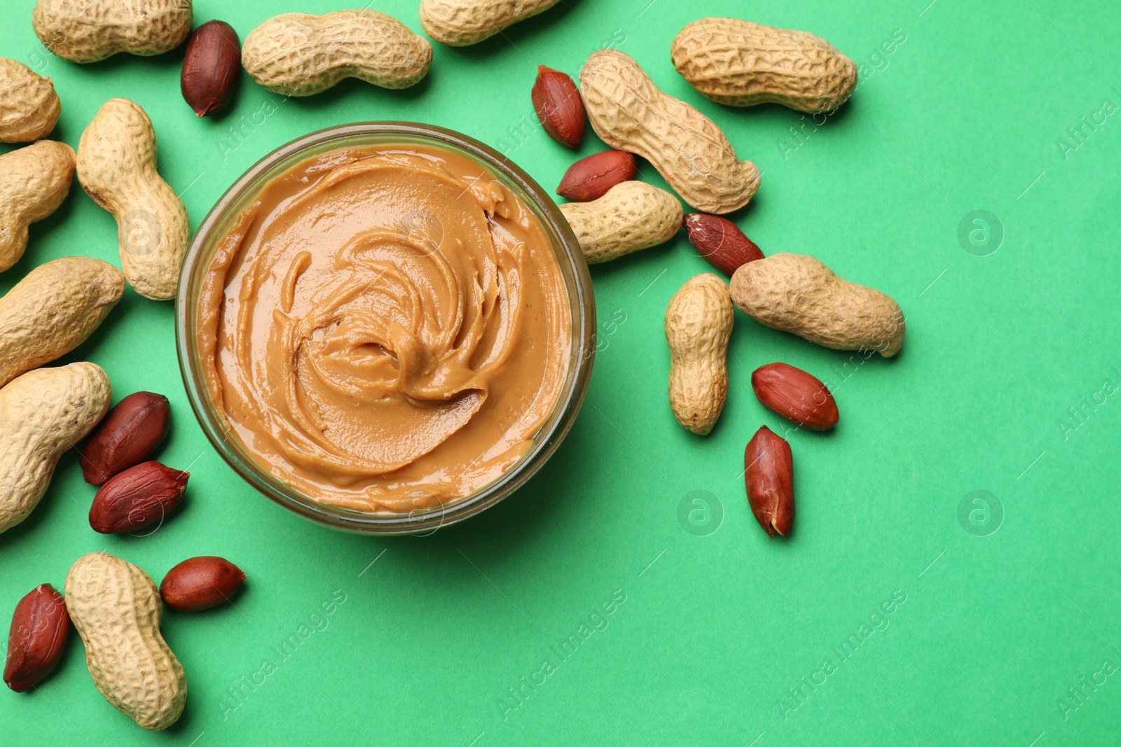 Photo of Tasty peanut butter in bowl and groundnuts on green background, flat lay