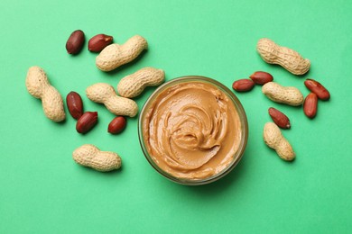 Photo of Tasty peanut butter in bowl and groundnuts on green background, flat lay