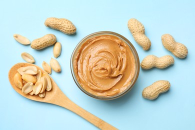 Photo of Tasty peanut butter and groundnuts on light blue background, flat lay