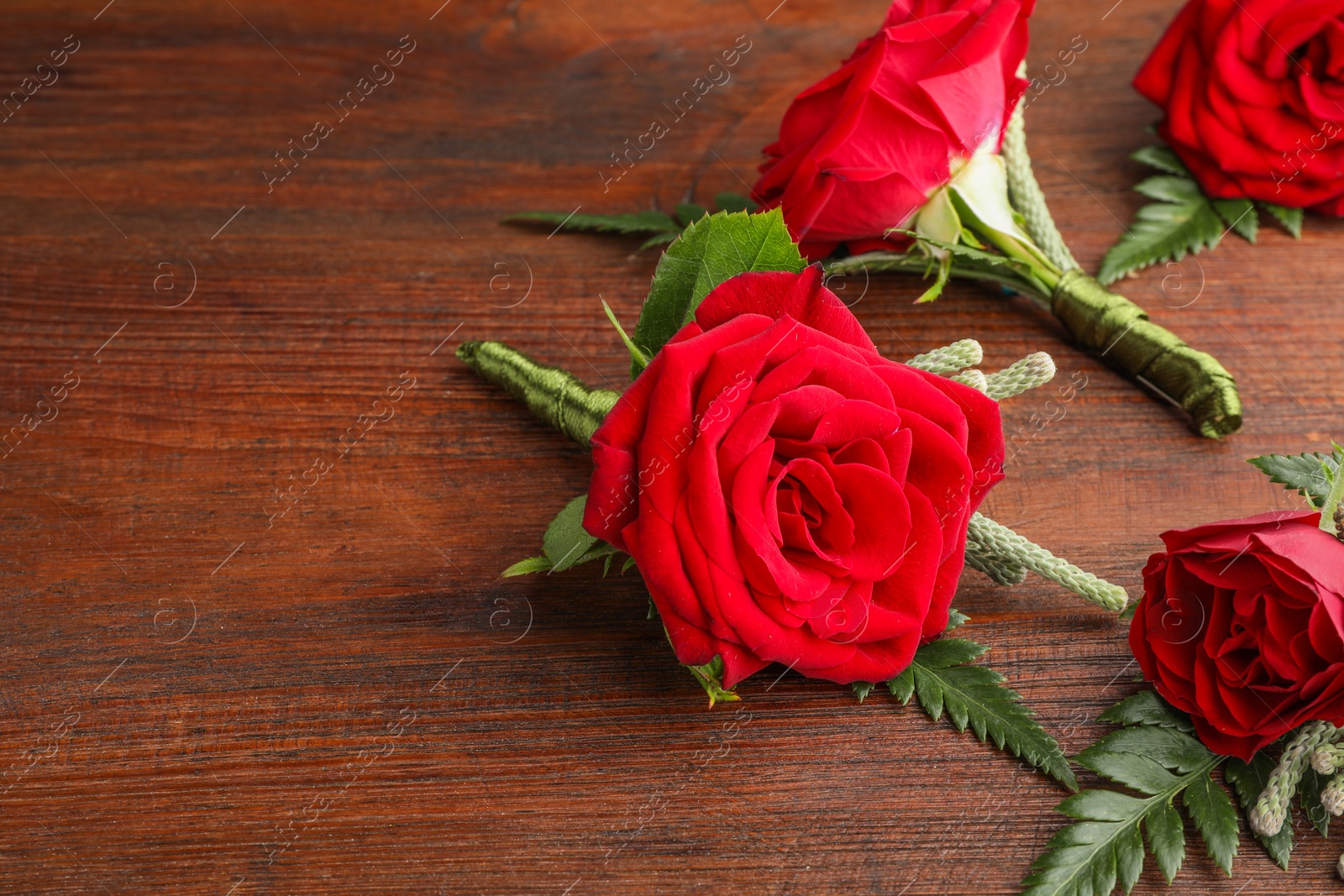 Photo of Many stylish red boutonnieres on wooden table, space for text