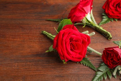 Many stylish red boutonnieres on wooden table, space for text