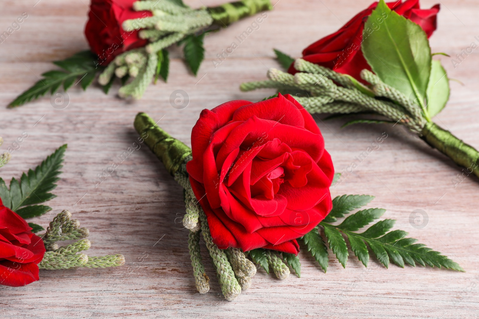 Photo of Many stylish red boutonnieres on light wooden table