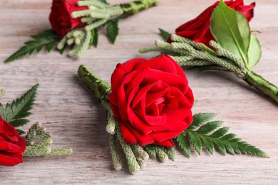 Many stylish red boutonnieres on light wooden table