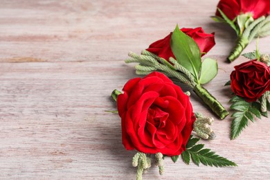 Many stylish red boutonnieres on light wooden table, space for text