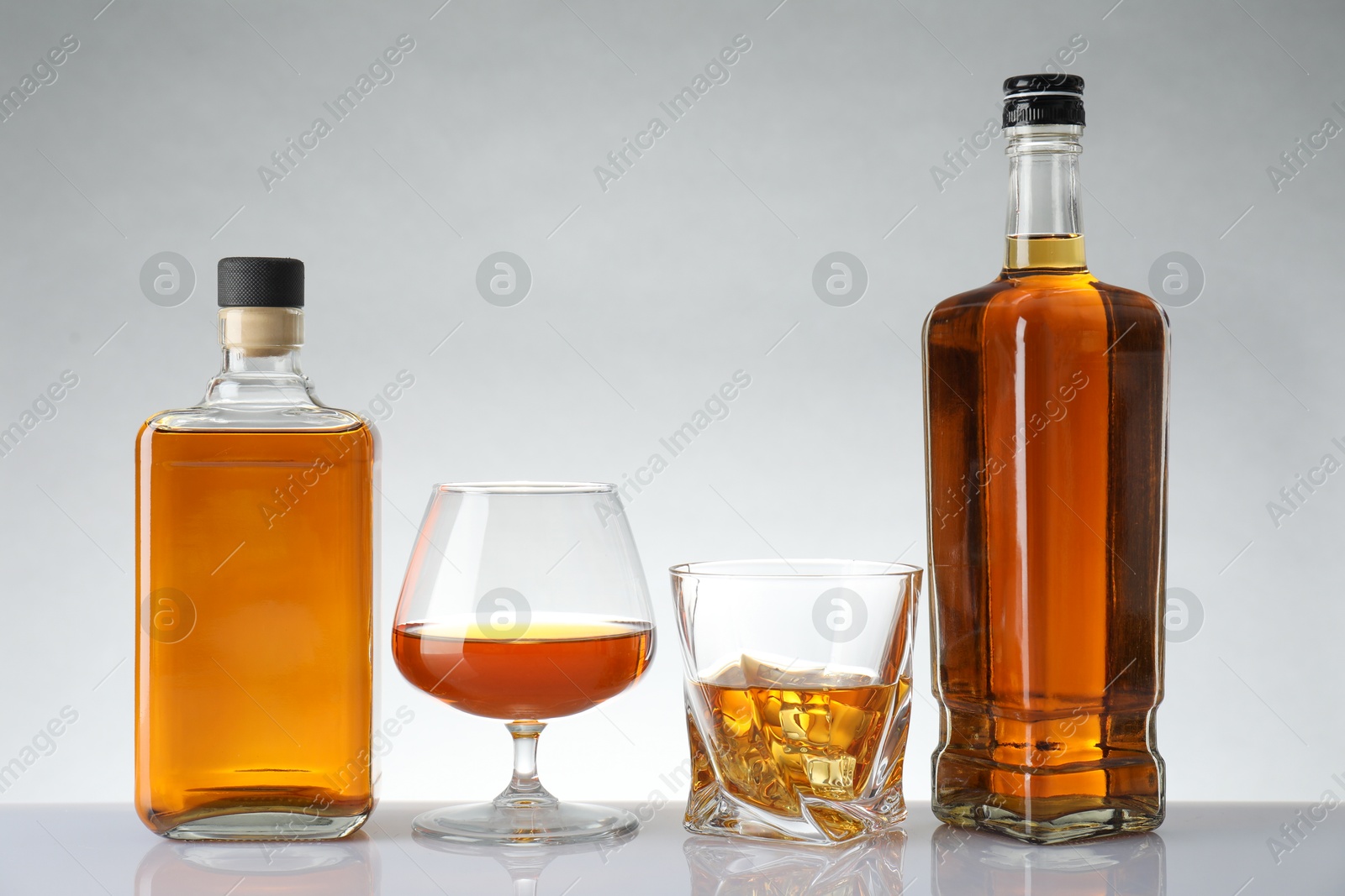 Photo of Bottles and glasses with different alcoholic drinks on white table against light background