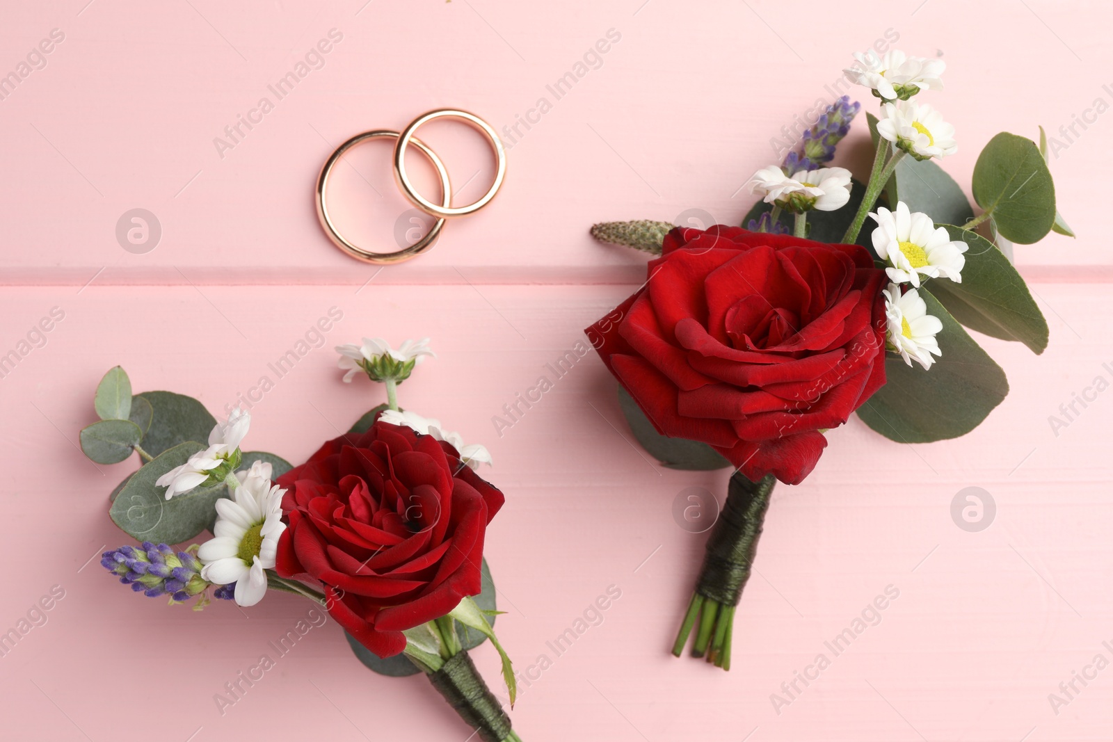 Photo of Stylish boutonnieres and rings on pink wooden table, flat lay