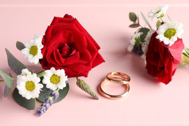 Stylish boutonnieres and rings on pink wooden table