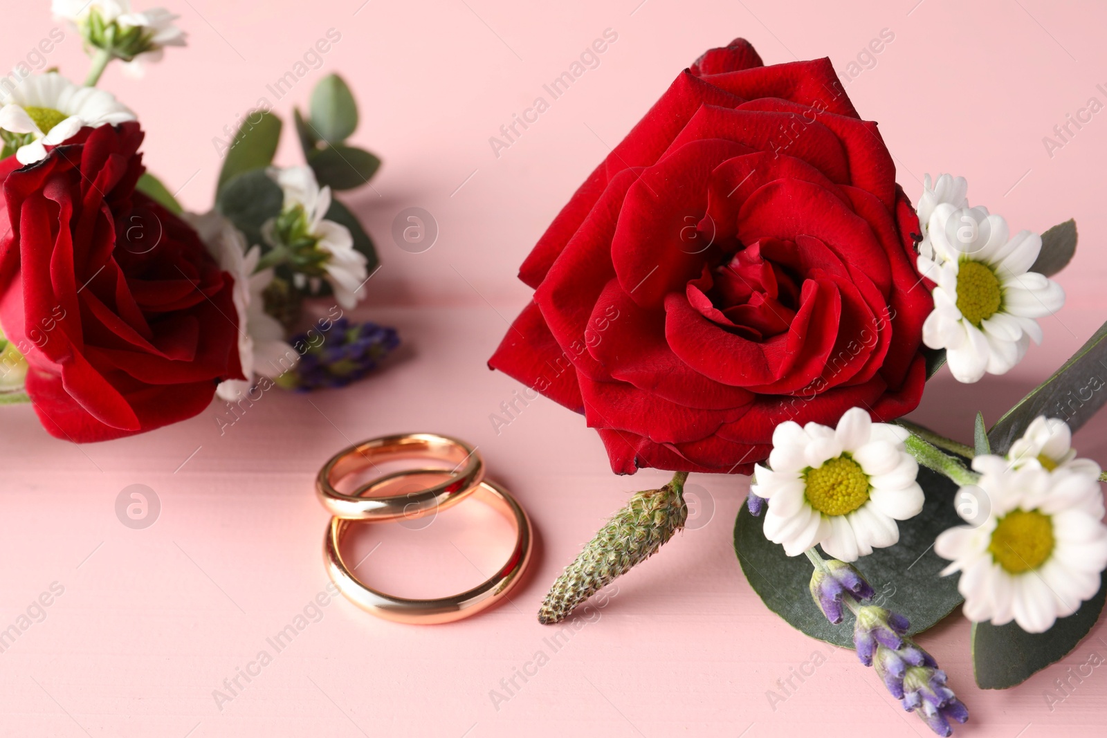 Photo of Stylish boutonnieres and rings on pink wooden table, closeup