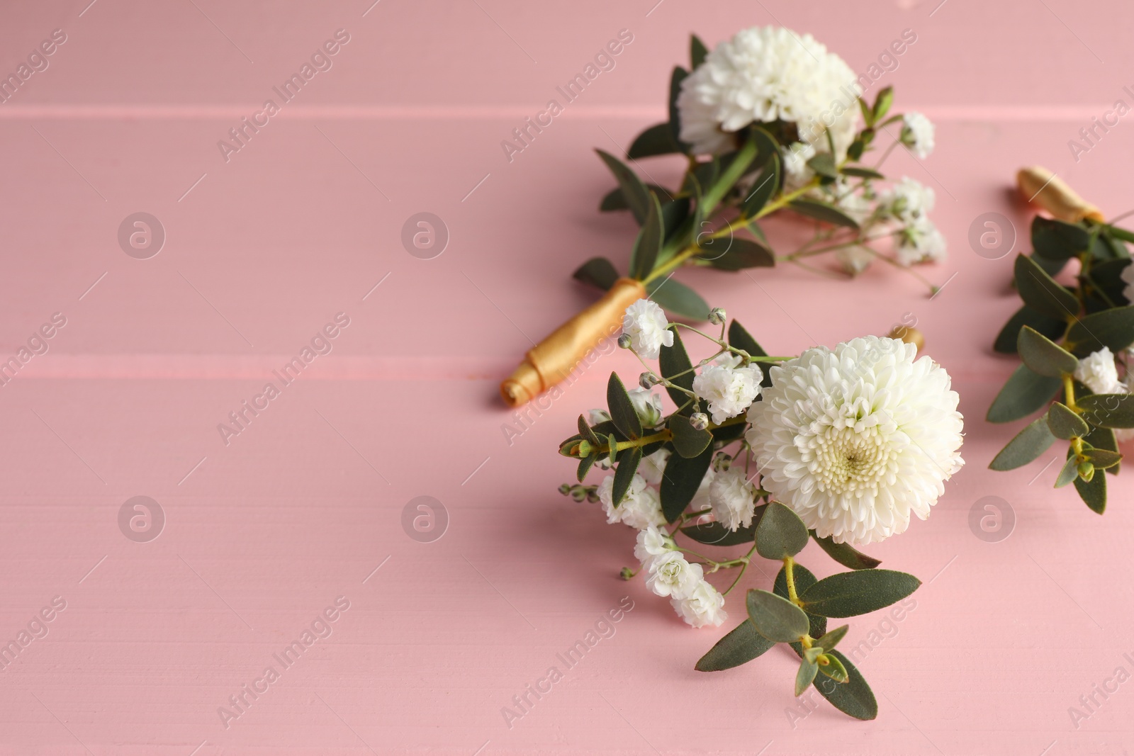 Photo of Many small stylish boutonnieres on pink wooden table. Space for text