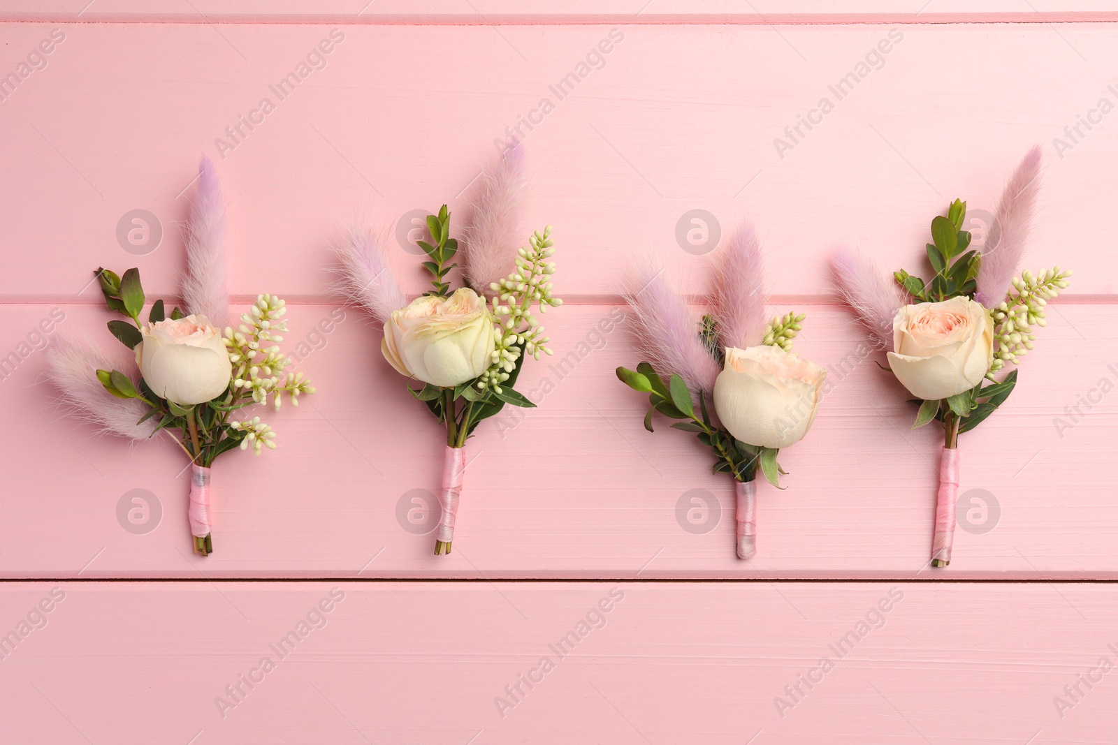 Photo of Many small stylish boutonnieres on pink wooden table, flat lay