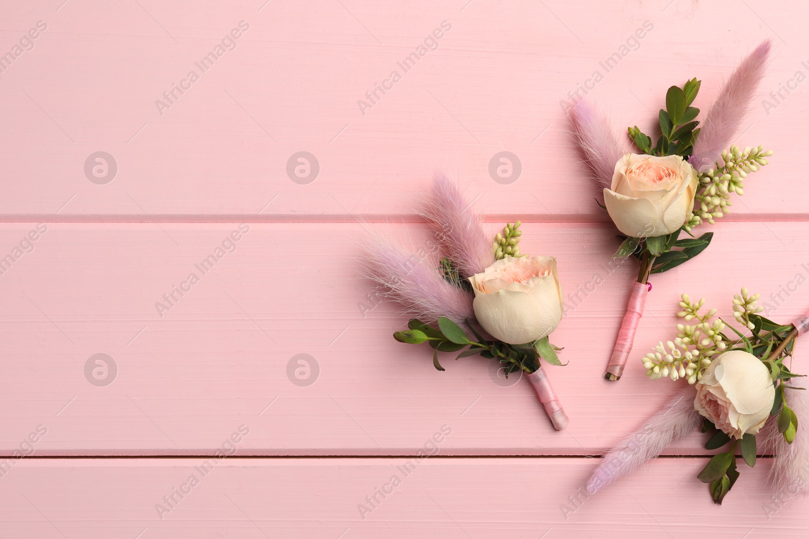 Photo of Many small stylish boutonnieres on pink wooden table, flat lay. Space for text