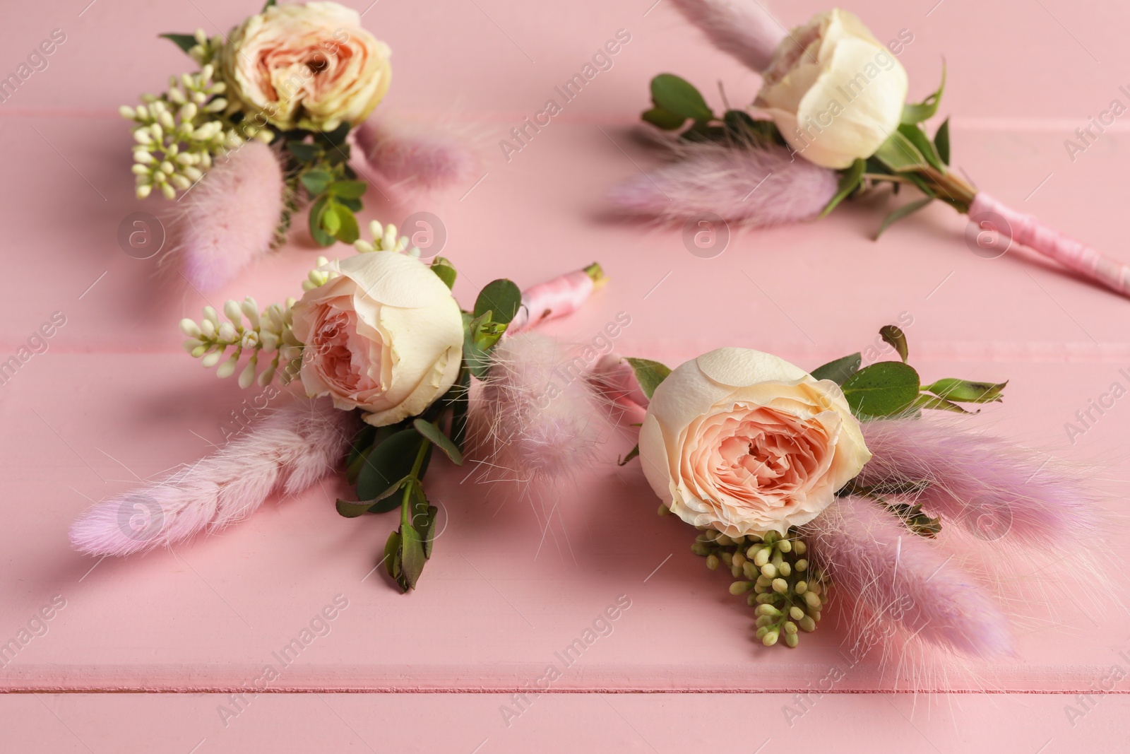 Photo of Many small stylish boutonnieres on pink wooden table, closeup