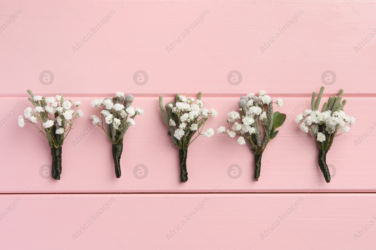 Photo of Many small stylish boutonnieres on pink wooden table, flat lay