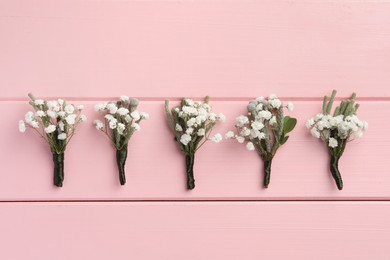 Many small stylish boutonnieres on pink wooden table, flat lay