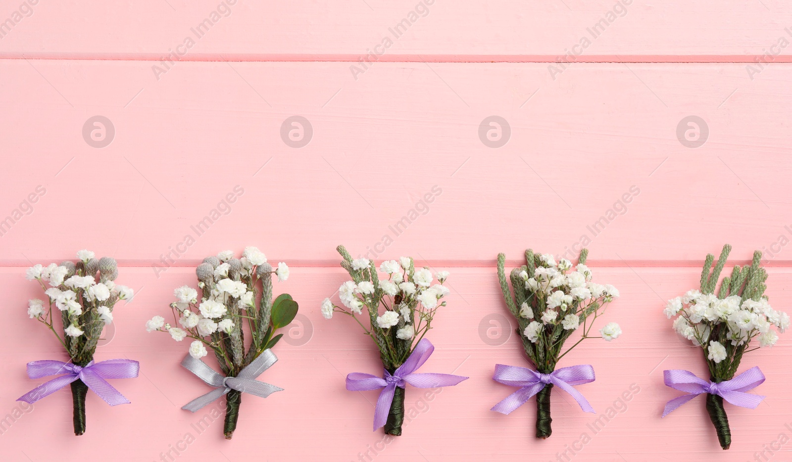 Photo of Many small stylish boutonnieres on pink wooden table, flat lay. Space for text