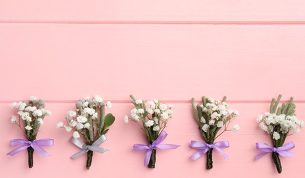 Photo of Many small stylish boutonnieres on pink wooden table, flat lay. Space for text