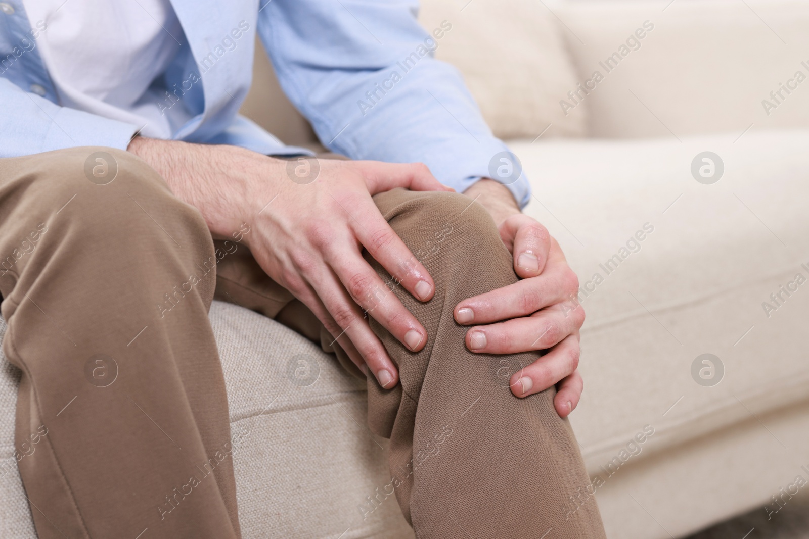 Photo of Man suffering from knee pain on sofa indoors, closeup