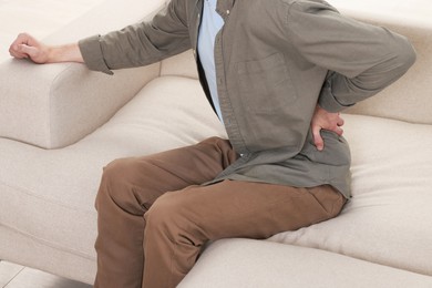Photo of Man suffering from back pain on sofa indoors, closeup