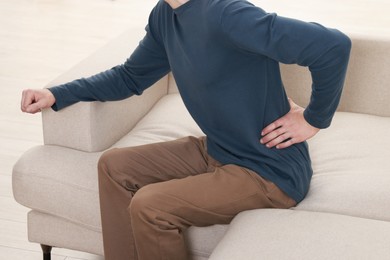Photo of Man suffering from back pain on sofa indoors, closeup