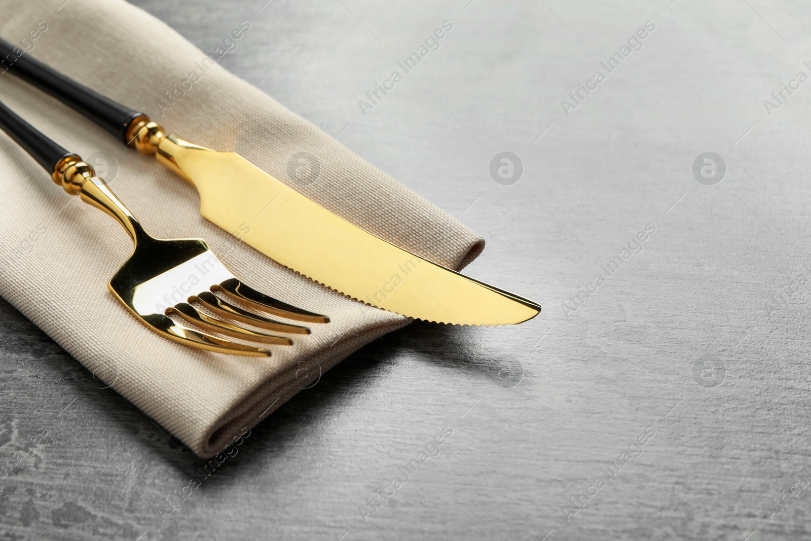 Photo of Elegant golden cutlery and napkin on grey table. Space for text