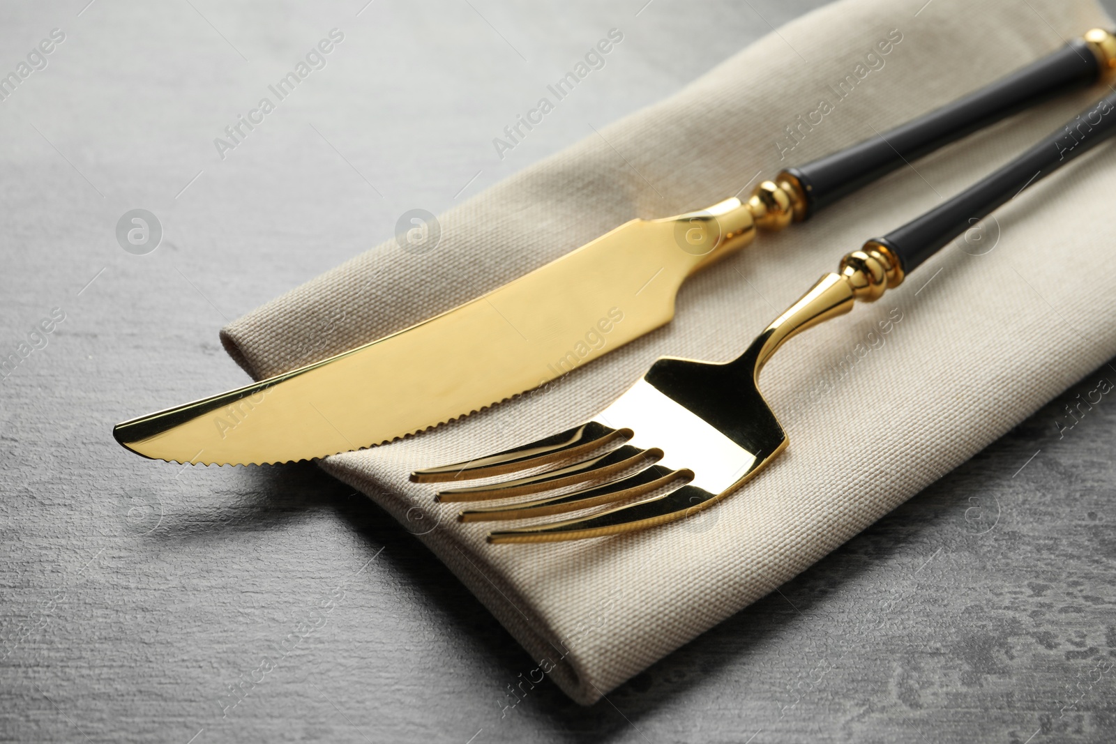 Photo of Elegant golden cutlery and napkin on grey table, closeup