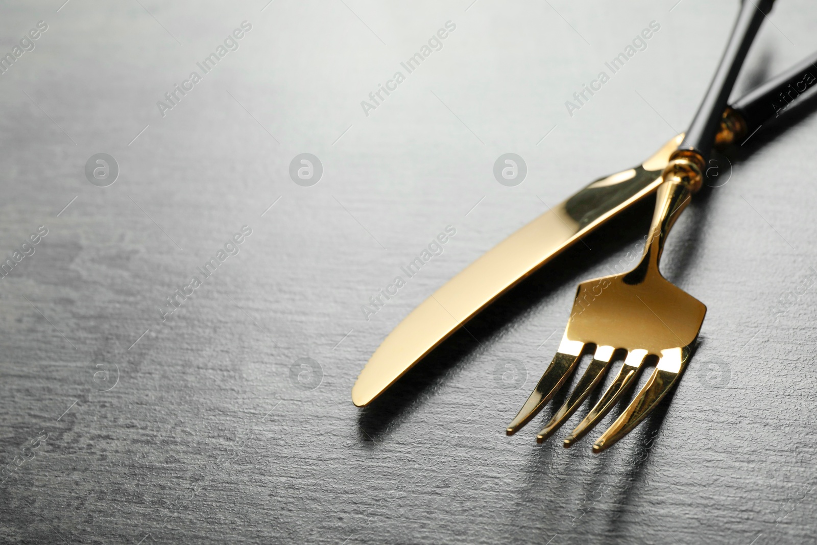 Photo of Stylish cutlery. Golden knife and fork on grey table. Space for text