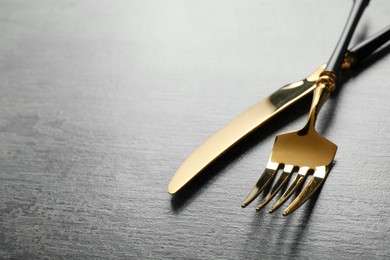 Stylish cutlery. Golden knife and fork on grey table. Space for text