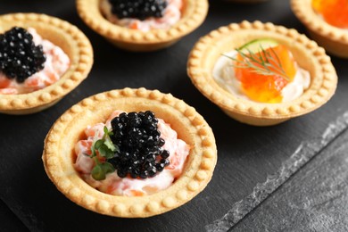 Delicious canapes with salmon and caviar on black table, closeup